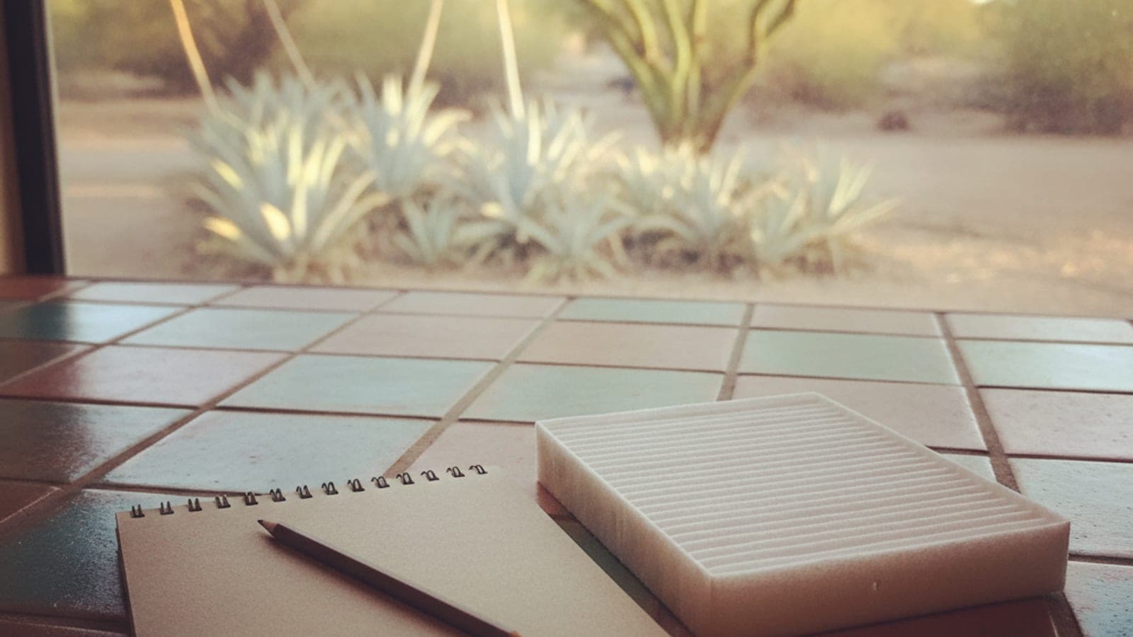 Una libreta y una pluma sobre la barra de una cocina luminosa en una casa de Tucson, con una ventana que da a un jardín de desierto