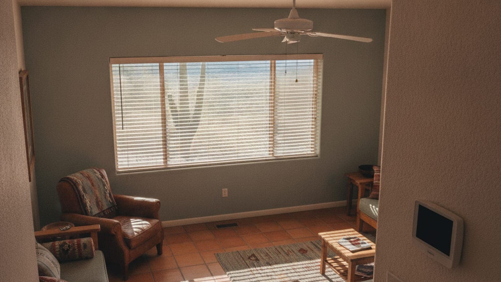 Una sala en Tucson con las persianas medio cerradas, un ventilador de techo y un termostato en la pared una tarde de verano