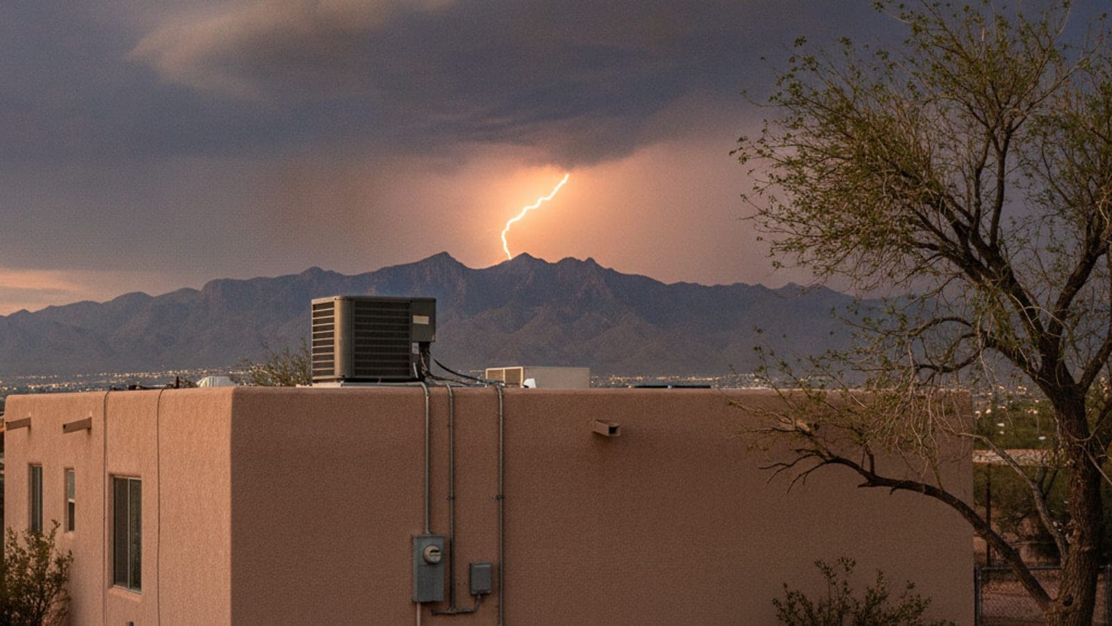 Nubes de tormenta del monzón con rayos a lo lejos sobre un vecindario de Tucson y una casa de estuco con techo plano y un condensador de aire acondicionado